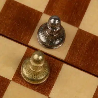Dos peones dorado y plateado uno frente al otro sobre el tablero de caoba