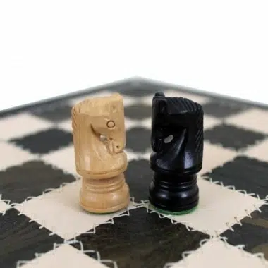 Detalle de los dos caballos en madera clara y negra sobre el tablero de cuero